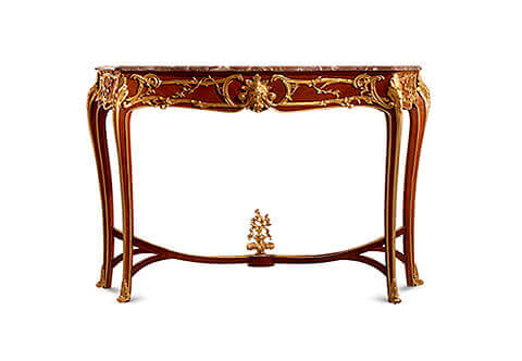 A prodigious French 19th Century Belle Époque Louis XV Rococo style gilt-ormolu-mounted freestanding Console Table after the model by François Linke, The beveled marble top of serpentine outline above an undulating frieze centered by a finely chased ormolu  female mask with acanthus leaves headdress and foliage volutes within C-scroll and leafy encadrements repeated on the sides; Raised on angular cabriole legs surmounted by large acanthus leaves chutes, bordered with ormolu trim and ending in foliate scroll sabots, joined by an ormolu mounted inverted curved double X stretcher centered by a platform surmounted by a finial of an urn of prosperity surmounted by scrolling leaves, The original console table, with a mandolin player centering the stretcher and rococo acanthus mounts, although designed in the Louis XV style, is not fully developed in combining this style with the Art Nouveau style for which François Linke is renowned. Linke drew his inspiration from the extravagant Rococo creations of François de Cuvilliés (1695-1968) that can be seen in the engravings of Johann Michael Hoppenhaut in the 1750's